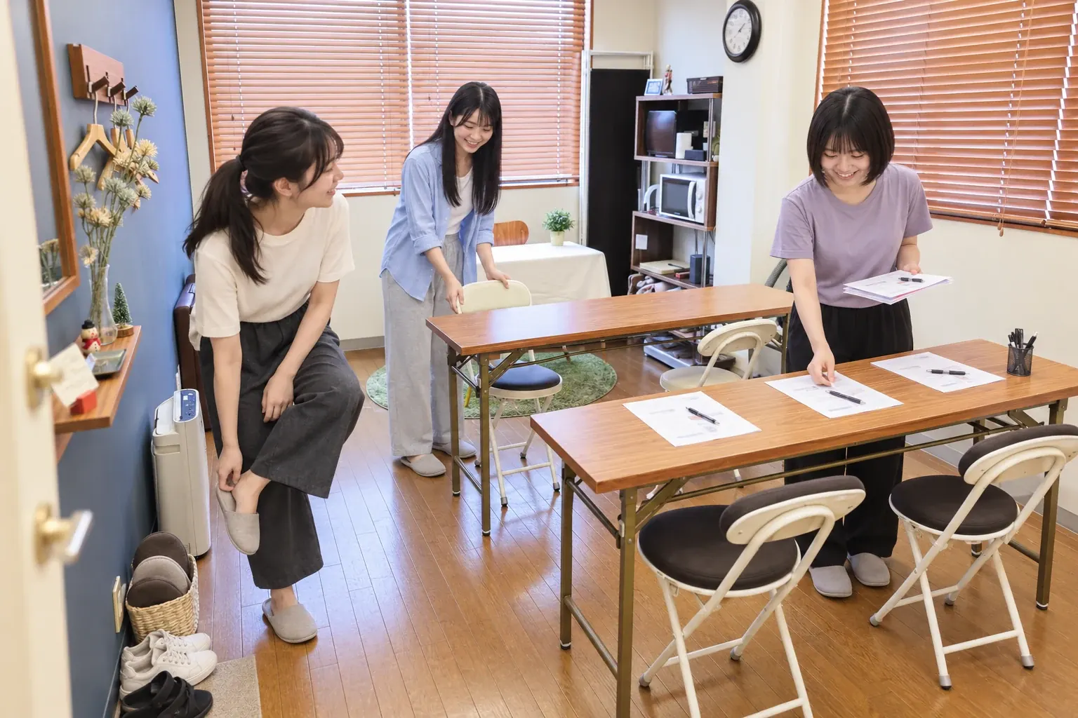 女性3人がスリッパに履き替えて入室し、ミニセミナーの机と資料を準備する利用イメージ
